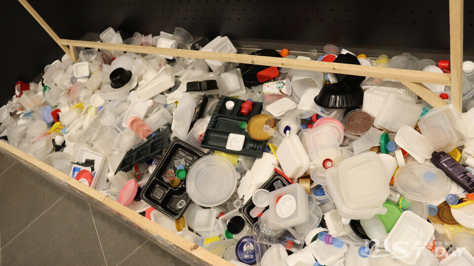 ‘1분 동안 버려지는 플라스틱의 양’이라는 안내문 아래에 다양한 종류의 플라스틱이 쌓여있다. (사진=배지인 기자)